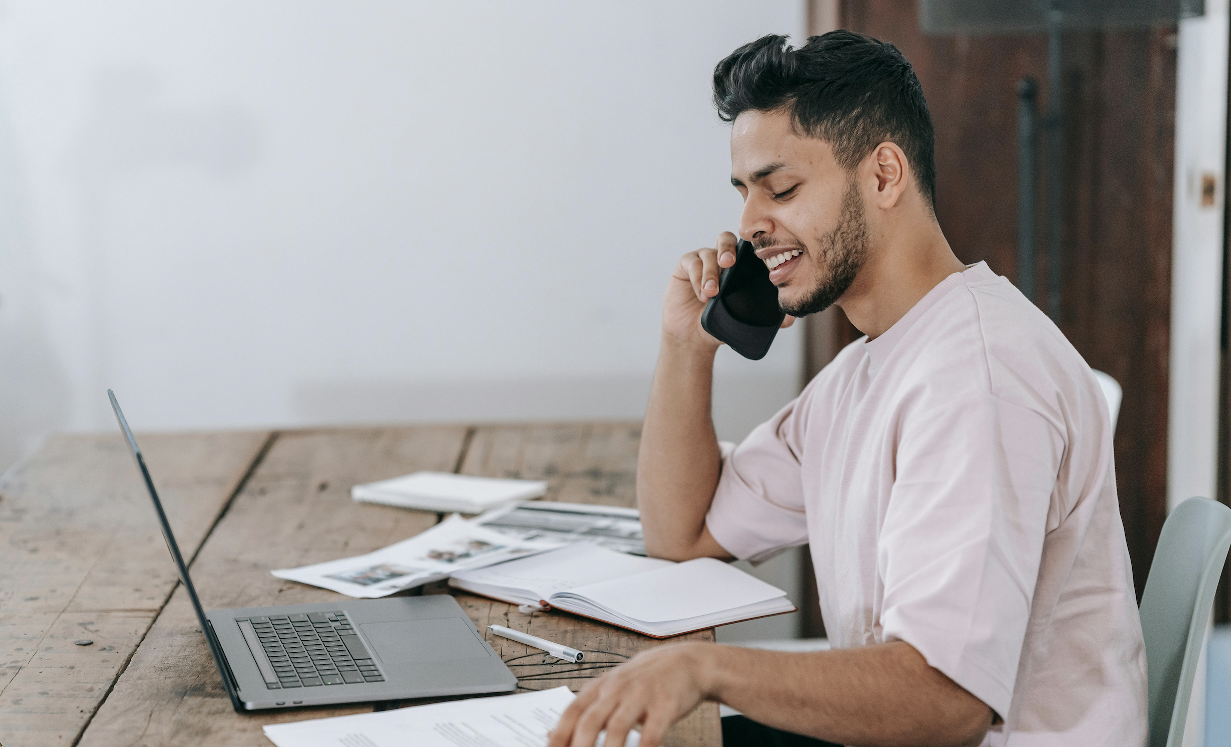 Man smiling while speaking on the phone in front of his computer.